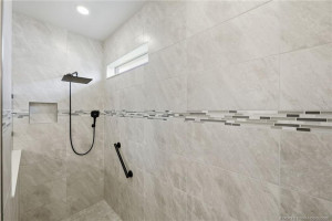 Oversized walk-in primary shower showcases elegant floor-to-ceiling tile, designer accent trim, built-in niche, and upgraded rainfall showerhead. This beautifully finished spa-inspired space offers a luxurious and relaxing retreat with modern style and exceptional attention to detail.