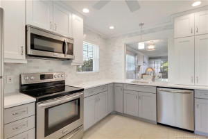 Beautifully renovated kitchen featuring soft gray shaker cabinetry, quartz countertops, tiled backsplash, stainless steel appliances, recessed lighting, and an open pass-through design perfect for entertaining.