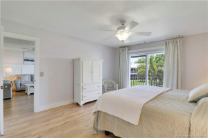 Relaxing primary bedroom retreat with private lanai access, beautiful natural light, wood-look flooring, and serene views of the lush grounds and waterways.