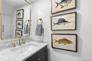 Updated half-bathroom features a marble-look vanity top, dark cabinetry, brass-tone fixtures, and a coordinating framed mirror.