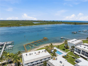 Aerial view showcases the community pool, waterfront grounds, sandy shoreline, and dock area.