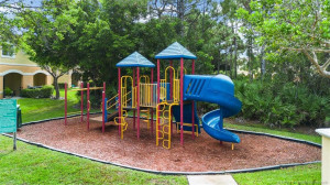 Kids love this colorful multi-level playset set in a wood-chip mulched area and set next to a grassy lawn and tropical foliage.