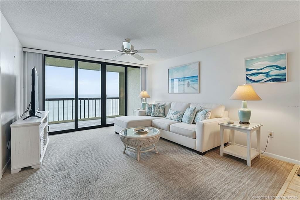 Oceanfront living room with floor-to-ceiling sliding glass doors opening to the balcony and direct Atlantic Ocean views. Virtually staged.