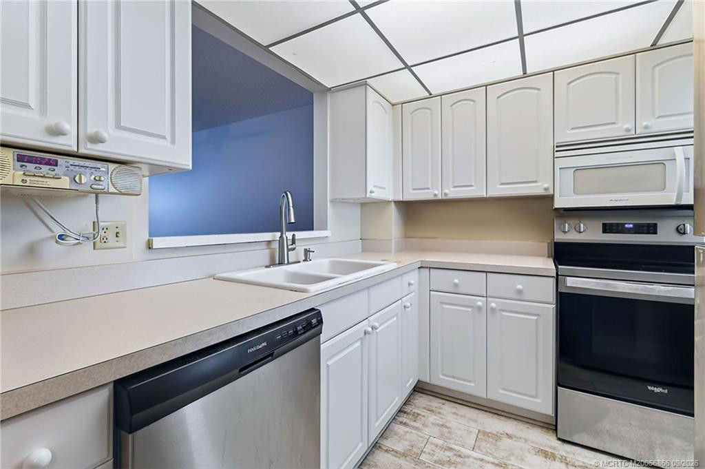 Kitchen with white cabinetry, ample counter space, stainless steel dishwasher and pass-through to the adjoining living area.