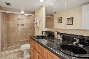Tiled walk in shower with double sinks on granite countertops