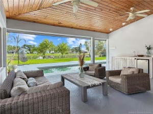 Expansive covered outdoor living area with beautiful wood ceiling, sink, and views of the sparkling pool and canal.