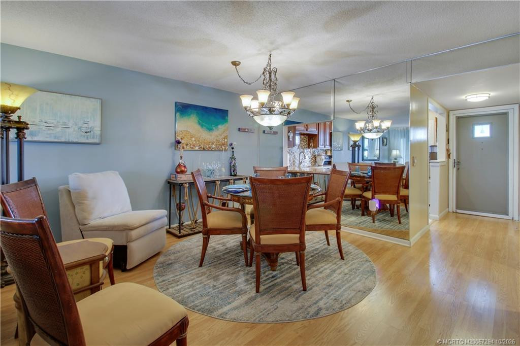 Lovely dining area featuring an elegant chandelier, decorative mirrored wall, and warm wood-look flooring. The mirrored wall reflects natural light and creates an open, airy feeling, while the kitchen's breakfast bar adds convenience.