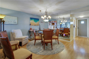 Lovely dining area featuring an elegant chandelier, decorative mirrored wall, and warm wood-look flooring. The mirrored wall reflects natural light and creates an open, airy feeling, while the kitchen's breakfast bar adds convenience.