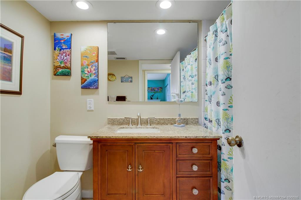 Attractive guest bathroom featuring a spacious granite-topped vanity, warm wood cabinetry, undermount sink, brushed-nickel fixtures, and a large wall mirror. Recessed lighting brightens the space.
