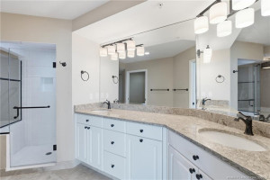 Spacious primary bathroom featuring dual vanities, granite countertops, and a glass-enclosed walk-in shower.