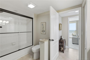 Convenient Jack-and-Jill bathroom featuring a tub/shower combination with glass enclosure, neutral tile flooring, and access from adjoining rooms.