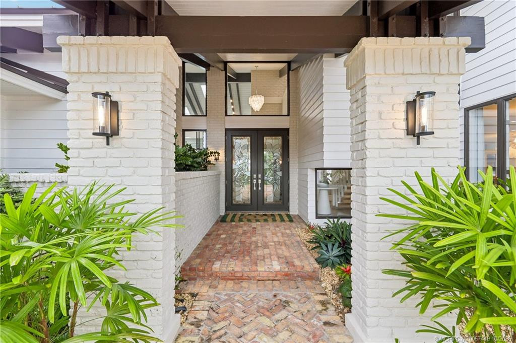 A dramatic entry framed by painted brick columns, architectural beams, and elegant double doors