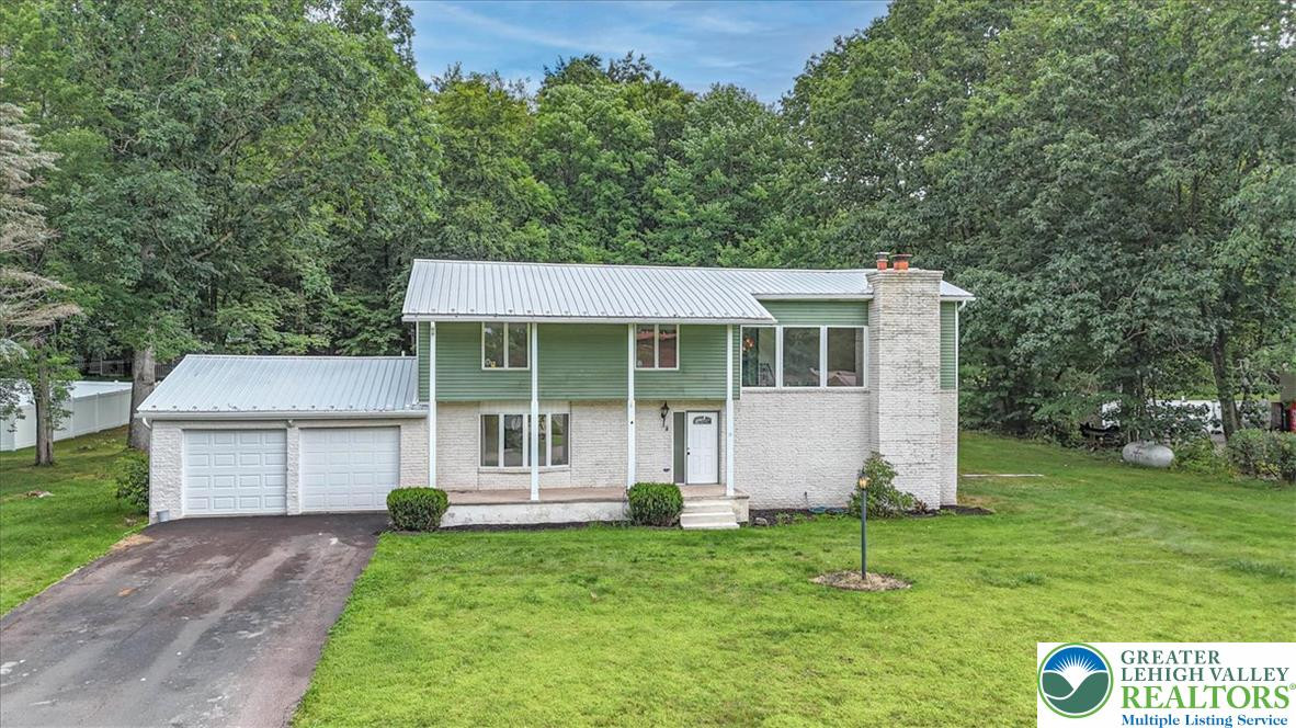Mature trees frame a classic split-level exterior featuring a brick facade and metal roof. Mature trees frame a classic split-level exterior