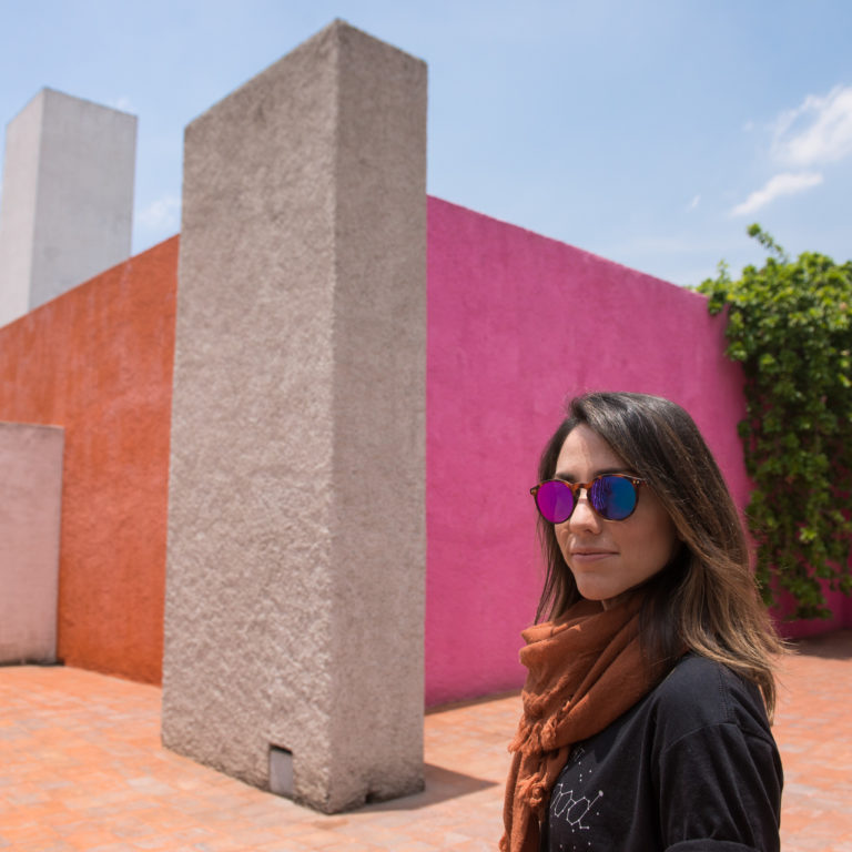 Sonia Gil, founder of Fluenz, standing next to the bold geometric walls of Luis Barragán’s iconic architecture in Mexico City, where vibrant pink and neutral tones create an atmosphere of modern Mexican design, a highlight of the Fluenz Spanish Immersion cultural experience.
