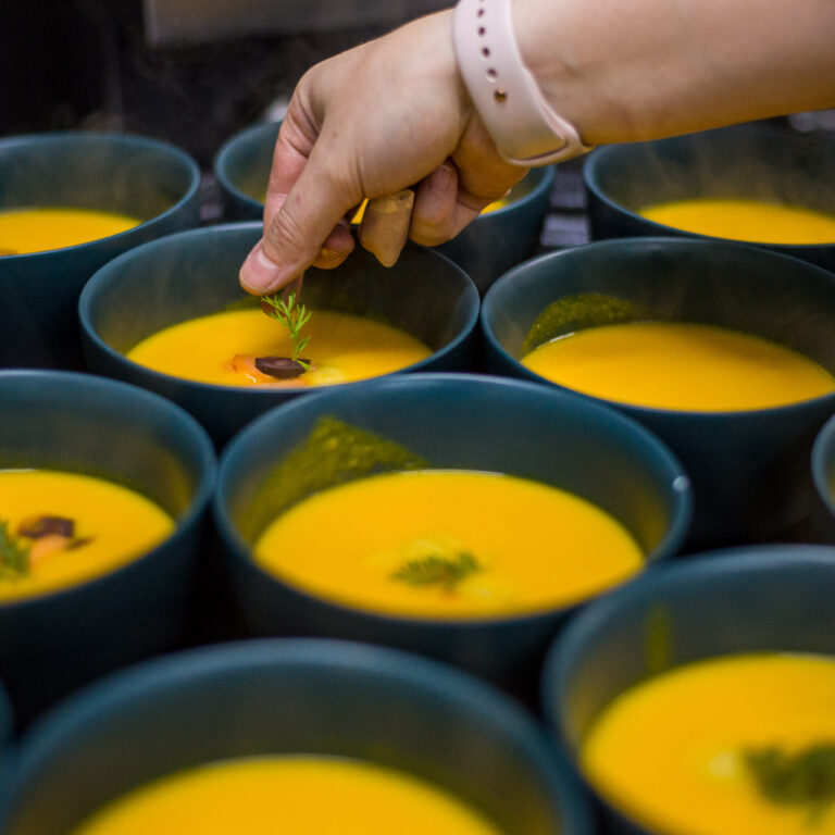 A chef carefully garnishing bowls of freshly made carrot soup during a private dining experience at the Fluenz Spanish Immersion in Mexico City, where learners and coaches share gourmet meals as part of the cultural and linguistic immersion.