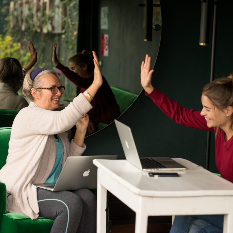 A Fluenz Spanish Bootcamp learner and coach celebrate progress with a high-five during a one-on-one session, laptops open as they work through the program’s intensive, personalized Spanish training.