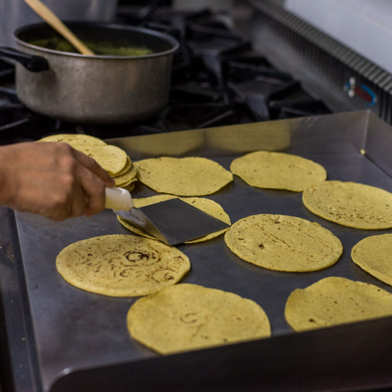 Fresh corn tortillas cooking on a hot griddle, showcasing how traditional Mexican cuisine is integrated into the cultural experience of the Fluenz Spanish Immersion in Mexico City.