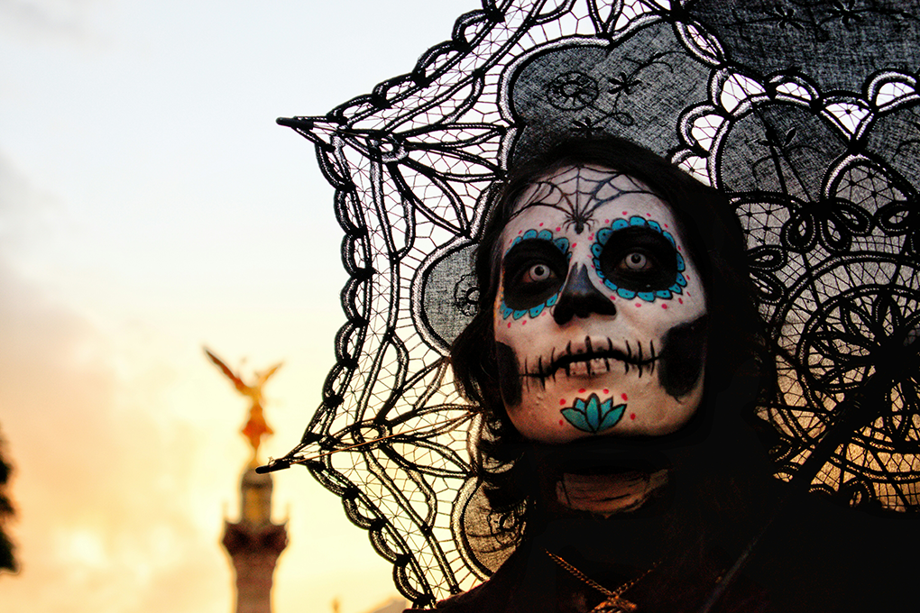 Day of the Dead celebration in Mexico City, featuring a woman with traditional Catrina face paint near the Ángel de la Independencia, an iconic cultural experience for learners in the Fluenz Spanish Immersion program.