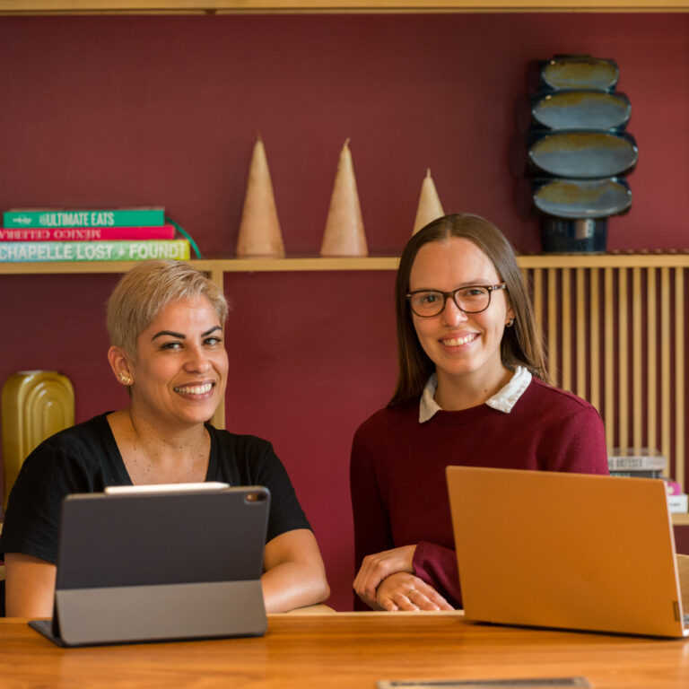 Spanish coach and adult learner during a personalized one-on-one session at the Fluenz Spanish Bootcamp in Mexico City. Both are seated at a modern table with laptops, smiling in a relaxed, elegant environment that reflects the immersive and high-end atmosphere of the program.