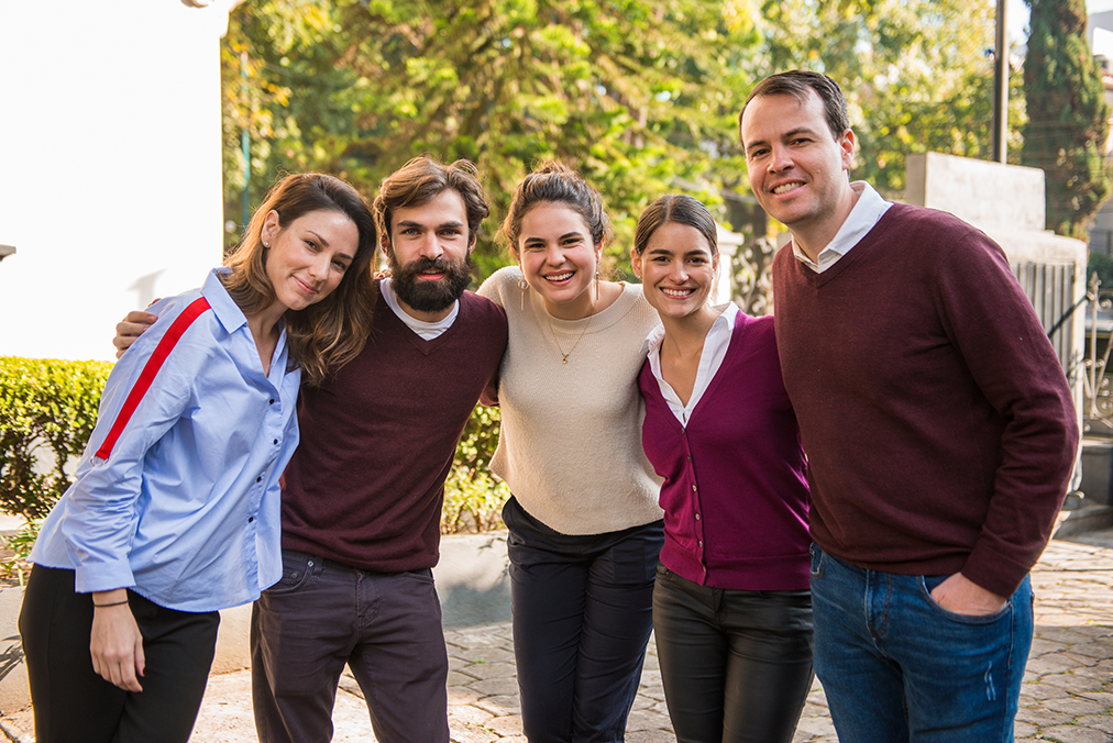 A group of Fluenz Spanish coaches collaborating outdoors in a tropical setting, representing the amazing team behind the Online Spanish Immersion. These expert instructors work together to design customized programs, deliver live one-on-one sessions, and guide learners toward fluency with a coordinated and highly personalized approach.