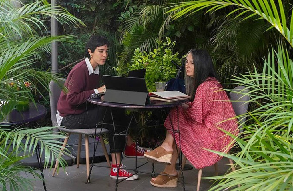 Spanish tutor and student working together outdoors at a small table surrounded by lush plants during the Fluenz Spanish Bootcamp in Mexico City; an intensive, one-on-one Spanish immersion experience offering the best and most effective program to learn Spanish in Mexico City.
