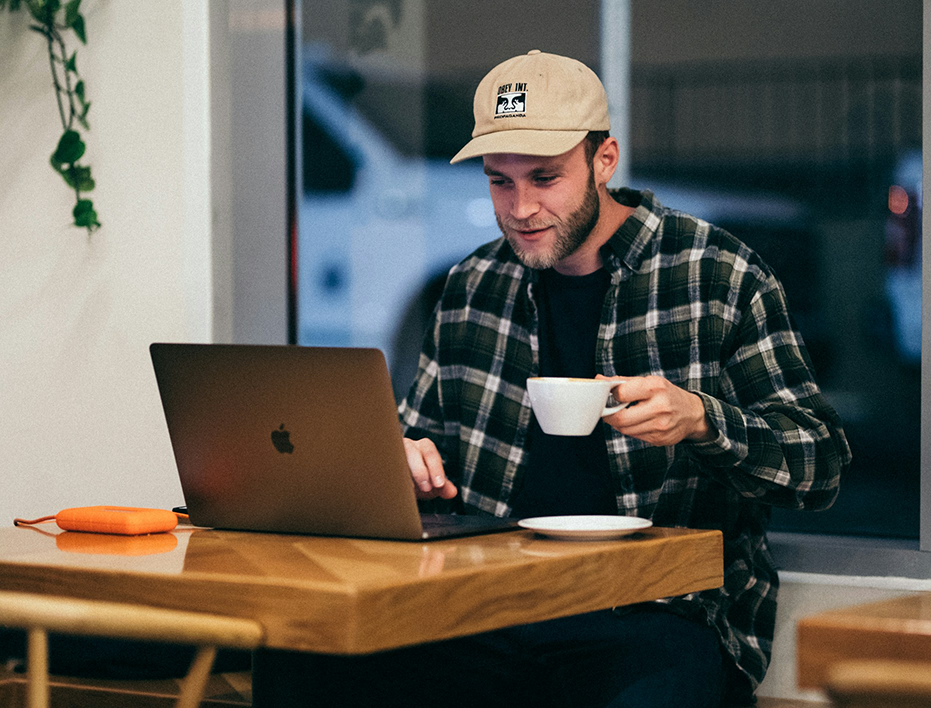 A student sits in a café with a laptop and a cup of coffee during his one-on-one online Spanish immersion session through Fluenz Live Online. An example of learning Spanish on Zoom with an intensive, structured approach, part of the best course to learn Spanish online in the world.