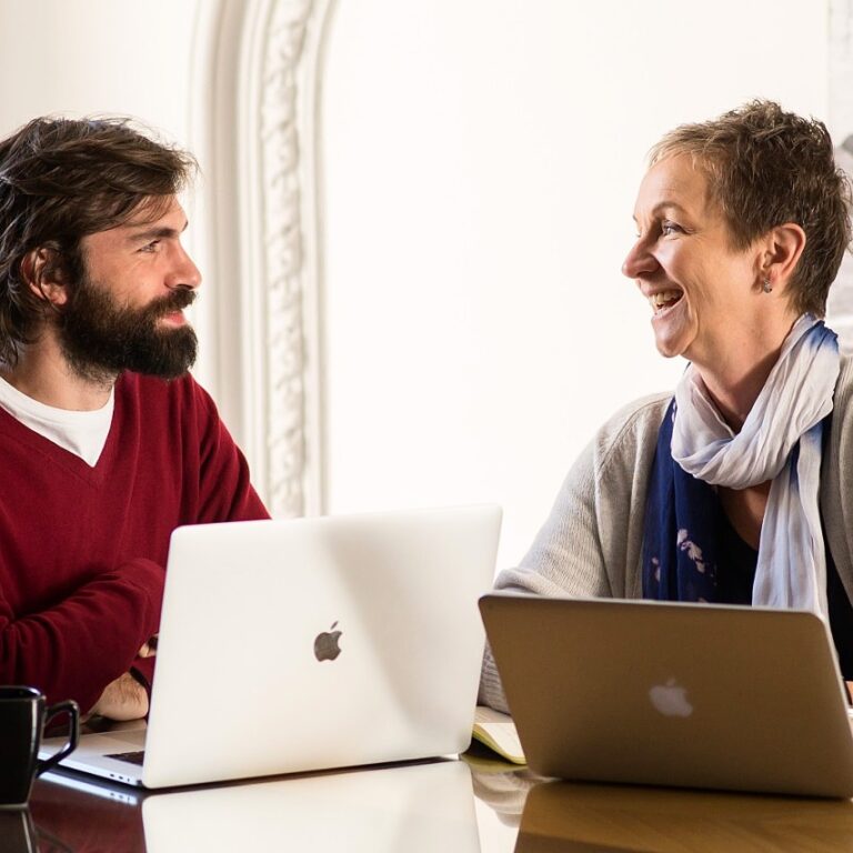 Spanish tutor and adult student working one-on-one at the Fluenz Spanish Bootcamp in Mexico City, both smiling during an intensive, personalized session with laptops open; best program to learn Spanish in Mexico City featuring the most effective and high-end Spanish learning environment.