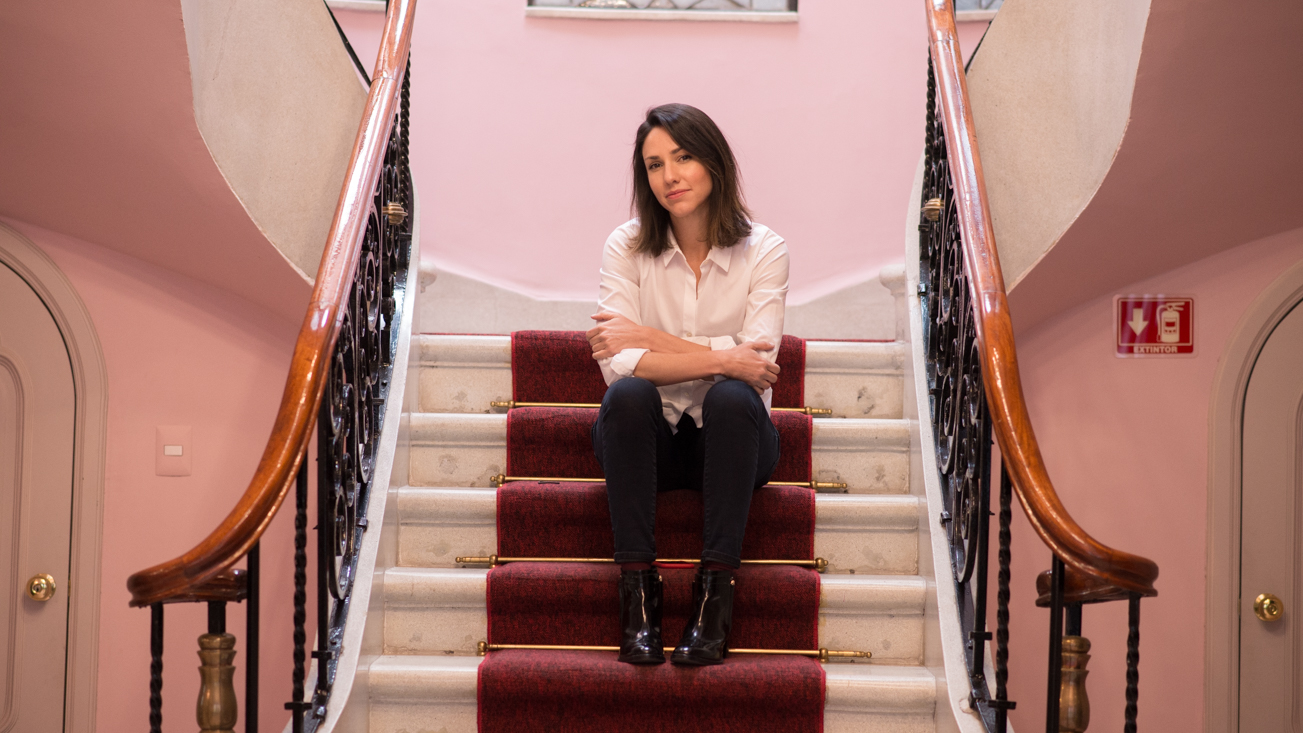 Sonia Gil, founder of Fluenz, sits on a red-carpeted staircase in a historic Mexico City building, illustrating the leadership behind Fluenz’s online Spanish immersion program—an intensive, one-on-one, live online Spanish learning experience designed for structured, efficient progress through the best Spanish course on Zoom in the world.