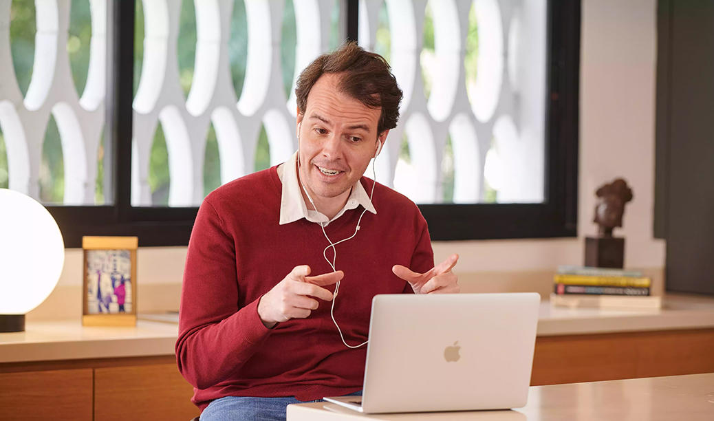 Spanish tutor in a burgundy sweater leading a Fluenz online Spanish immersion session, teaching one-on-one Spanish live online via laptop.