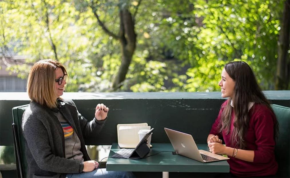 Adult learner and Fluenz Spanish tutor in a one-on-one Spanish Bootcamp session, working together outdoors with laptops and notebooks in a natural setting.