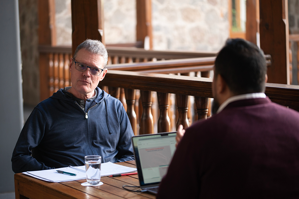 Adult learner in a one-on-one Fluenz Spanish immersion session in Puebla, working with a Spanish tutor at a wooden table with laptop and notebook in a historic courtyard setting.
