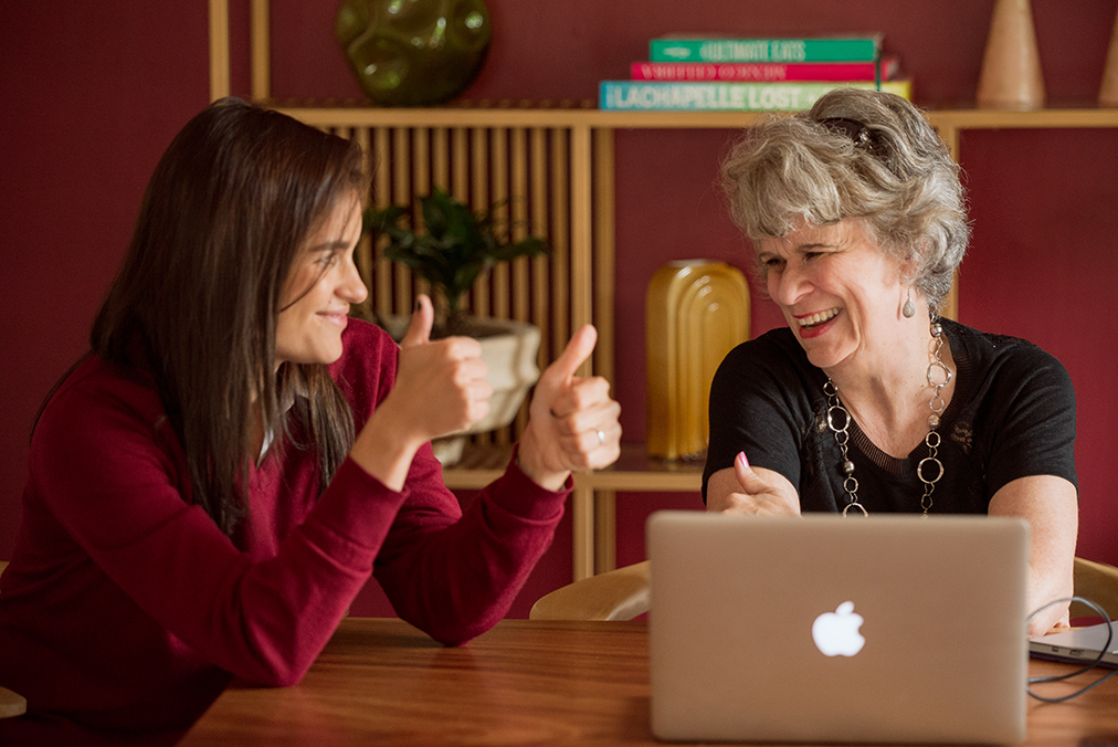 Spanish tutor and adult learner celebrating progress during a one-on-one Fluenz Spanish Bootcamp session, smiling and giving thumbs up across a table with a laptop in a warm, modern learning space.