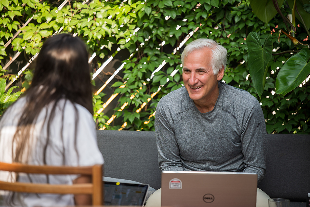 Adult learner engaged in a one-on-one Spanish coaching session during the Fluenz Spanish Bootcamp, seated outdoors with a tutor and laptop, highlighting personalized instruction and focused conversation in a garden setting.