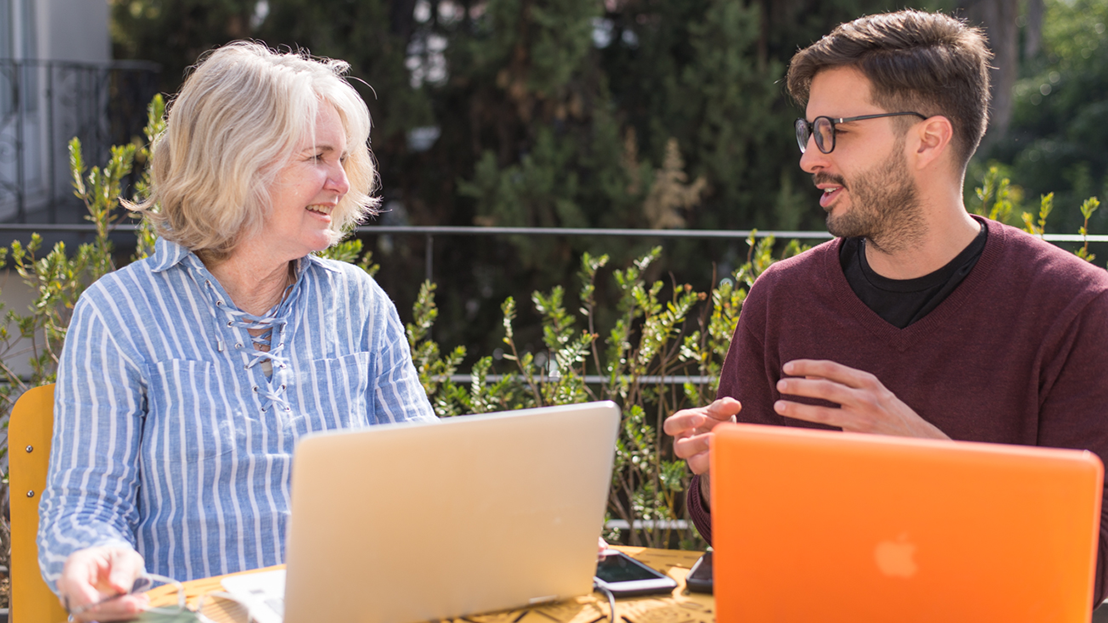 Adult learner and Spanish tutor in conversation during a one on one Fluenz Spanish Bootcamp session, working outdoors with laptops.