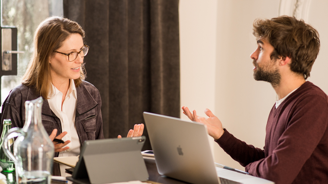 A Fluenz learner and coach work one-on-one during the Spanish Bootcamp, seated across from each other with laptops and a tablet, engaged in focused conversation in a bright, private setting.