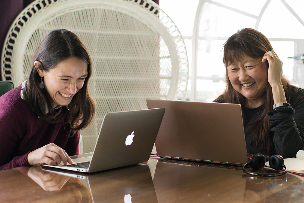 A Fluenz coach and learner share a moment of laughter during a one-on-one Spanish Bootcamp session, working closely on laptops in a focused yet engaging learning environment.
