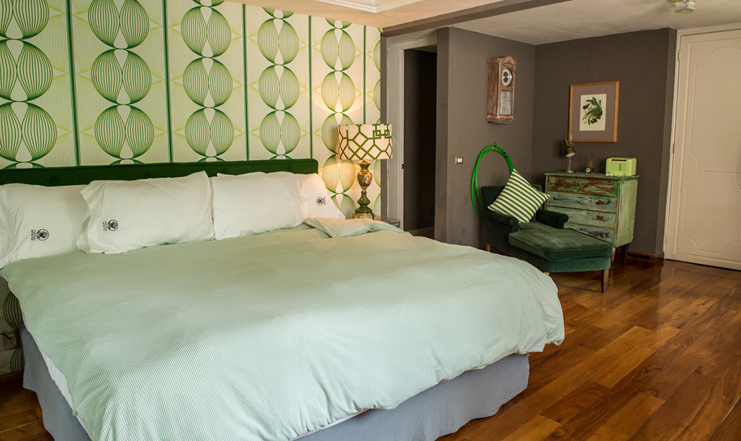 A stylish boutique hotel room in Mexico City featuring a king-size bed, patterned green wall design, and curated décor—part of the elevated accommodations included in the Fluenz Spanish Immersion experience.
