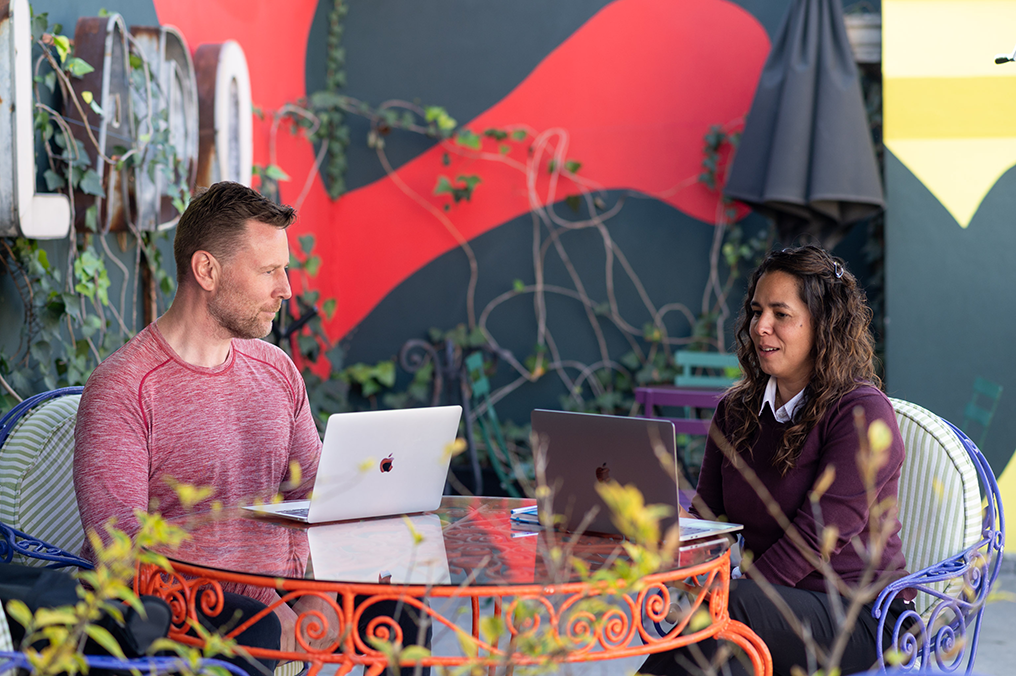 Adult learner in a one-on-one Spanish session with a Fluenz tutor in Mexico City, working together outdoors on laptops in a colorful courtyard.