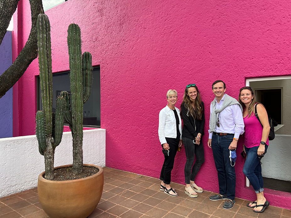 Adult learners from the Fluenz Spanish Immersion in Mexico City posing during a cultural outing, standing beside a cactus against a vibrant pink wall.