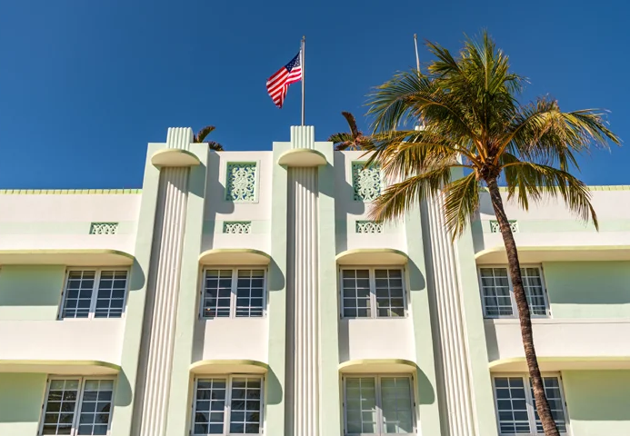 Art Deco building with palm trees and an American flag in Miami Beach, reflecting the vibrant setting of the Fluenz Spanish Bootcamp in Miami.