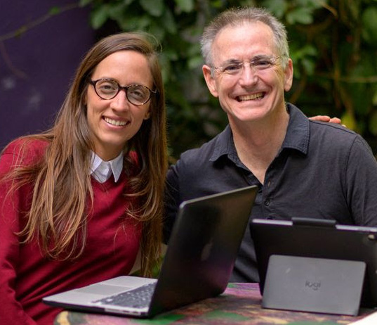 Fluenz Spanish Bootcamp participant smiles with his tutor during a one-on-one outdoor session with laptops.