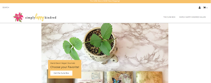 Simply Happy Kindred website screenshot showing a marble table with a plant and some notebooks.