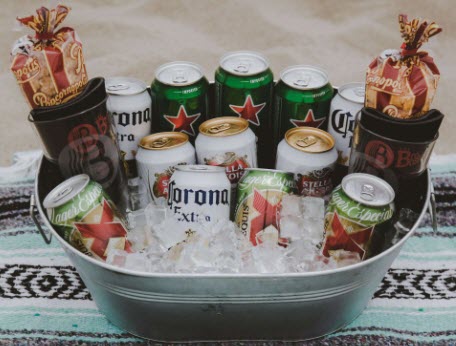 A metal tub with 12 cans of beer, beer glasses, popcorn and ice.