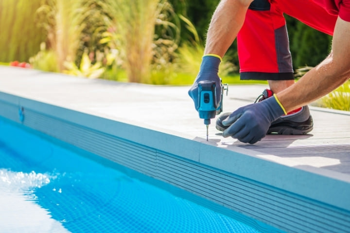 Installer fastening composite deck boards along the edge of a modern pool