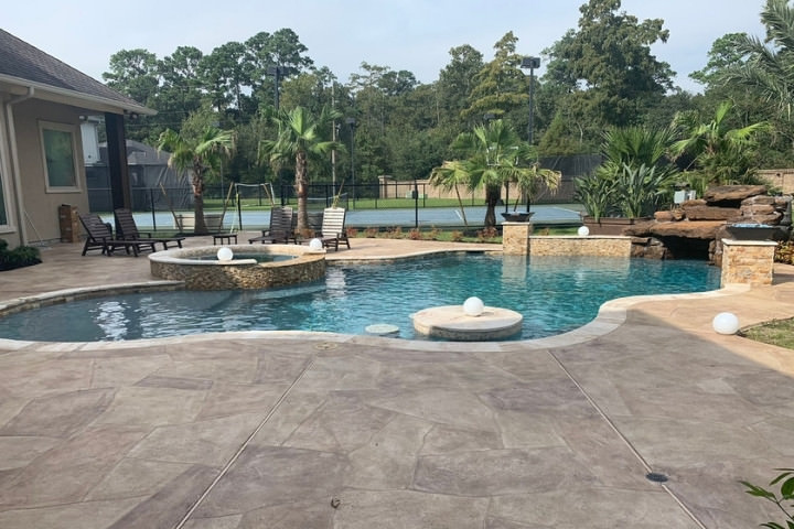 Freeform swimming pool framed by stamped concrete decking in a Houston backyard