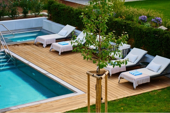Warm teak wood pool deck with lounge chairs beside a backyard pool