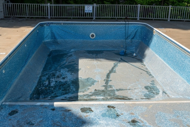 Worn in-ground pool interior showing surface damage that may require renovation
