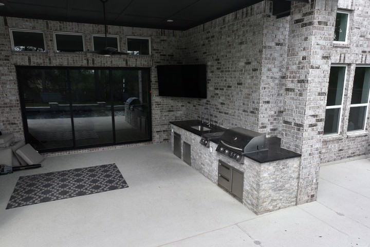 Covered patio outdoor kitchen featuring weather resistant brick, stone cladding, and stainless steel appliances