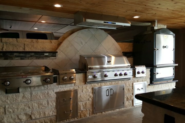 Covered rustic outdoor kitchen grill station with tiled backsplash detail, stone base, stainless grill, and smoker oven