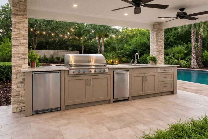 Neutral HDPE outdoor kitchen cabinetry paired with stainless steel appliances in a covered poolside entertaining space